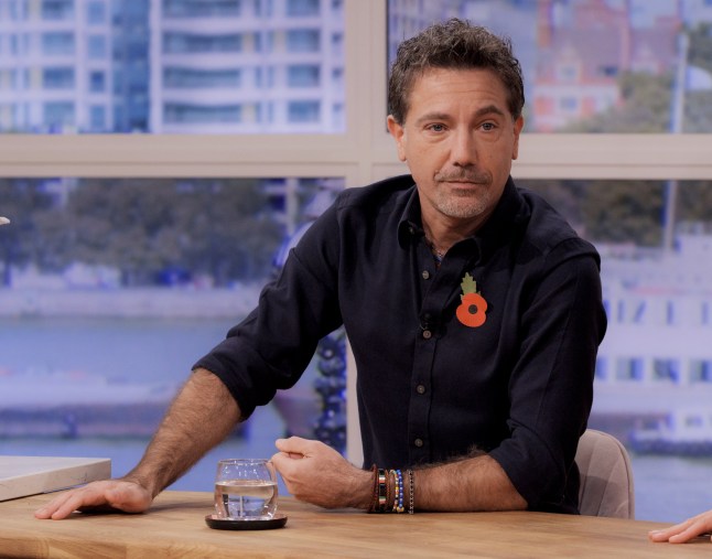 Gino D'Acampo sitting at a desk during an appearance on This Morning. He is wearing a navy blue shirt with a red poppy pin