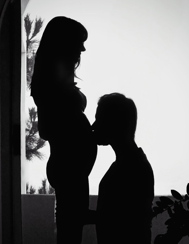 Silhouettes of Ioan Gruffudd and Bianca Wallace as he kneels to kiss her baby bump