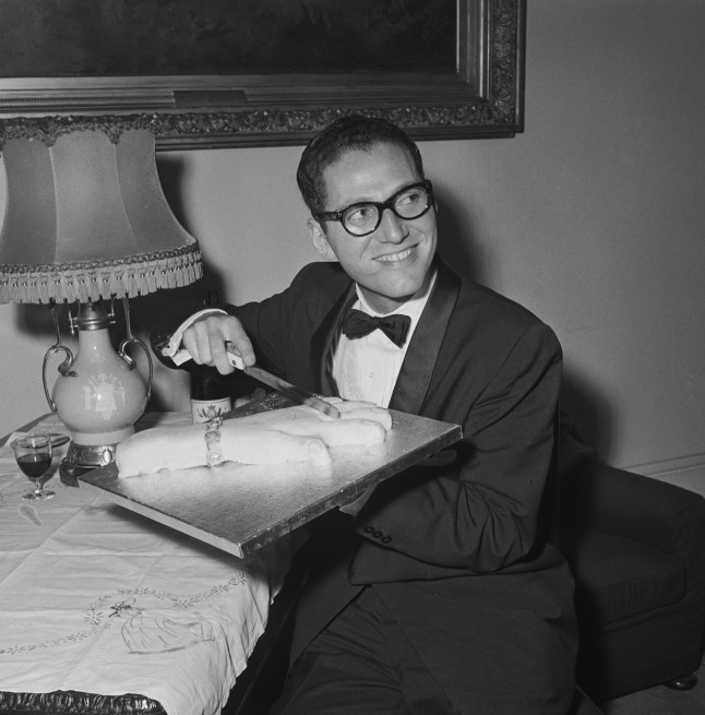 American satirical singer-songwriter, Tom Lehrer, cutting a cake in the shape of a woman's hand while backstage at the Palace Theatre, London, 13th May 1959. The cake alludes to Lehrer's macabre song, 'I Hold Your Hand in Mine'. (Photo by Evening Standard/Hulton Archive/Getty Images)