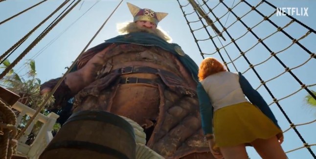 A still from the One Piece season two trailer of a woman looking up at a giant on a ship